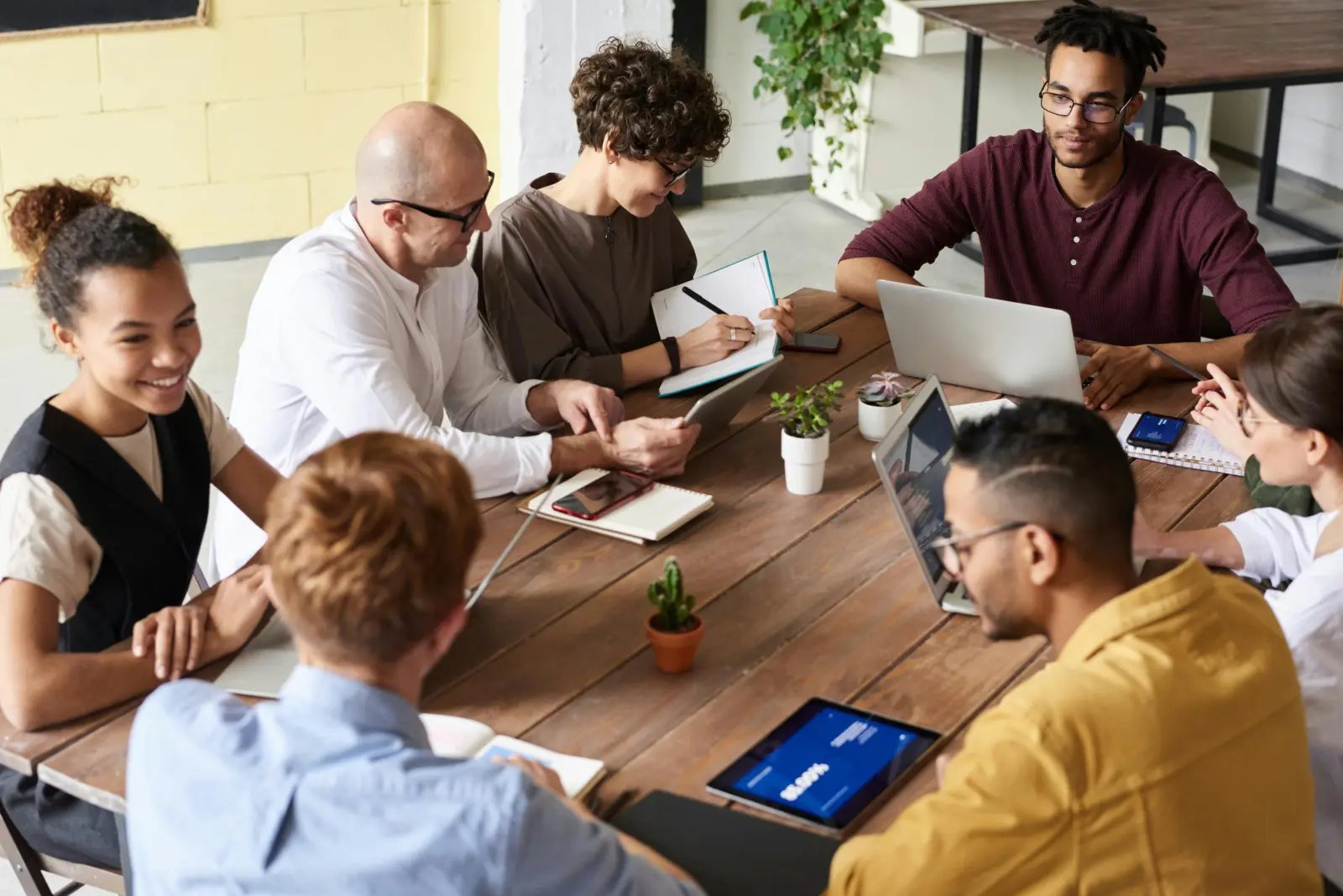Team members gathered around a wooden table reviewing work on laptops